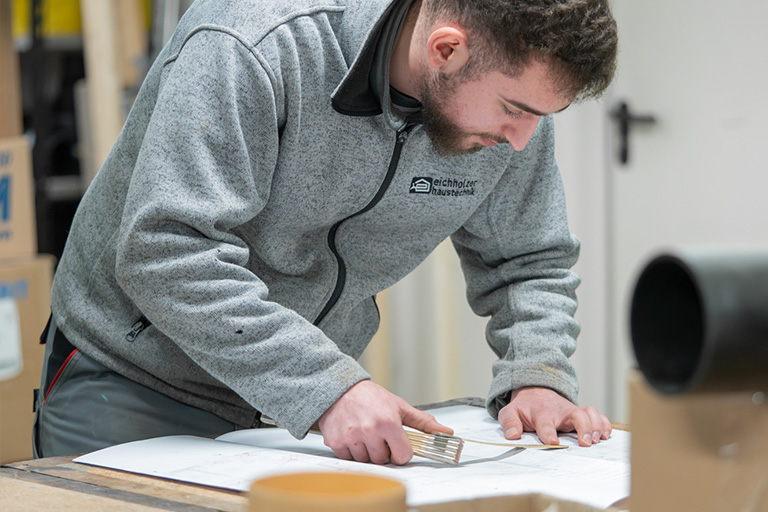 Mann mit Bart misst auf einem Plan etwas nach.