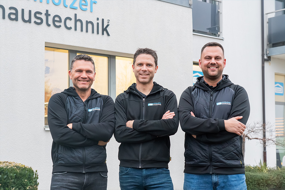 Drei Männer in Arbeitskleidung stehen vor Geschäftsgebäude und lächeln.