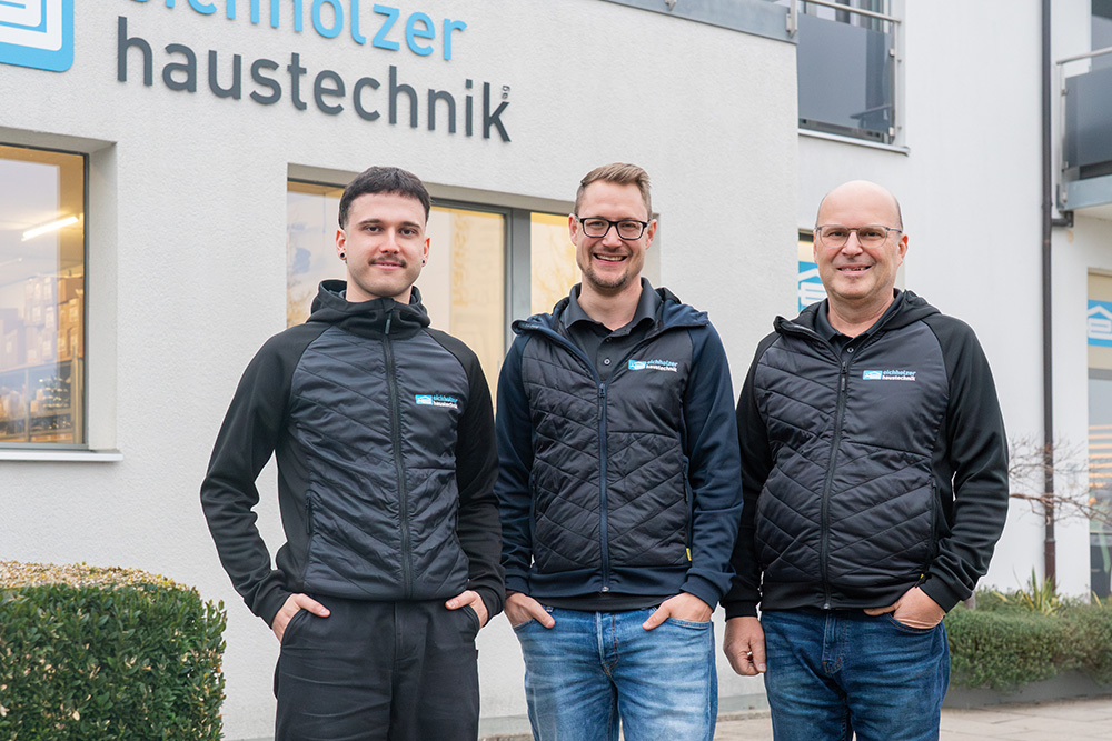 Drei Männer in Geschäftskleidung der Firma Eichholzer lächeln und stehen vor Geschäftsgebäude